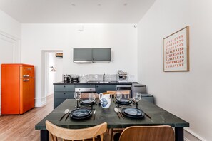A modern kitchen with a dining table set for two, a coffee machine, and a television above the counter. - Triangle d'Or — Elegance & King Size bed (Bordeaux)