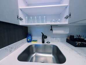 A modern kitchen with a stainless steel sink, white countertops, and a black faucet. - 1 Bdrm Gem: Walkable, Mins to Downtown, Queen Bed (Detroit)