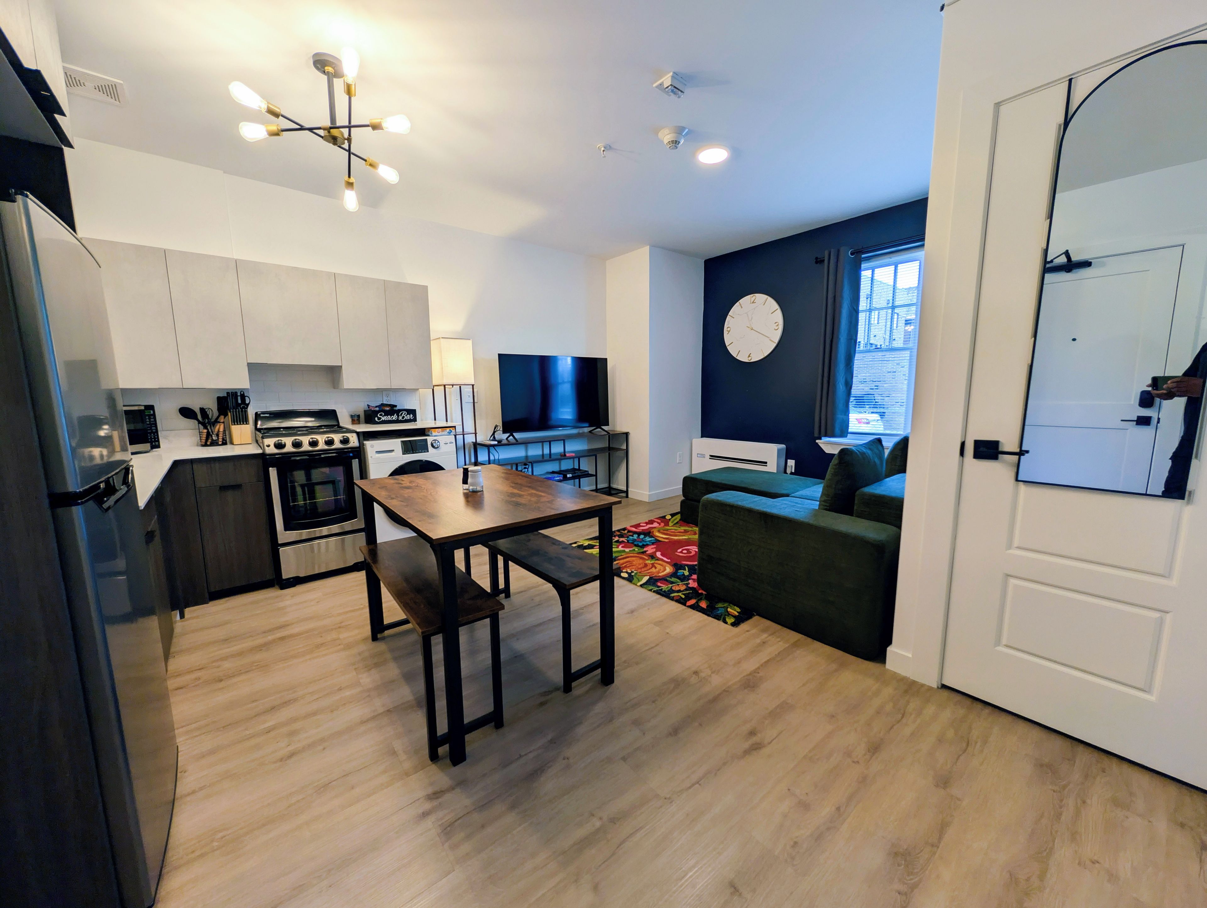 A modern kitchen with a dining area, a flat-screen TV, and a clock on the wall.