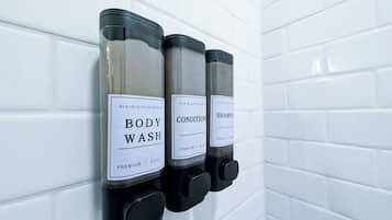 A wall-mounted dispenser with three bottles labeled 'BODY WASH,' 'CONDITIONER,' and 'SHAMPOO.'