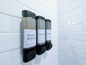 A wall-mounted dispenser with three bottles labeled 'BODY WASH,' 'CONDITIONER,' and 'SHAMPOO.' - 1 Bdrm Gem: Walkable, Mins to Downtown, Queen Bed (Detroit)