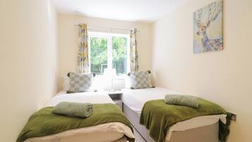 A bedroom with two beds, a window with curtains, a bedside table, and a painting on the wall.