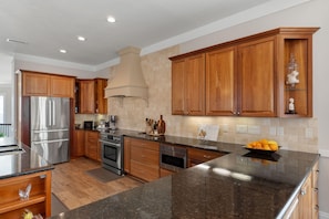 A modern kitchen with stainless steel appliances, wooden cabinets, and a granite countertop. - Luxury Soundfront Home in Gated Community with Water Views, Pool & Fire Pit (Navarre Beach)