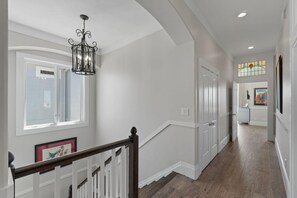 A hallway with a staircase, a chandelier, and a stained glass window. - Luxury Soundfront Home in Gated Community with Water Views, Pool & Fire Pit (Navarre Beach)