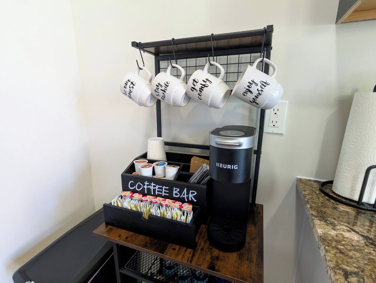A coffee bar setup with a Keurig coffee maker, a mug rack, and a coffee cup display.