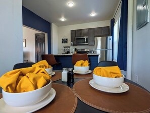 Een eethoek met een tafel gedekt voor vier personen, met witte kommen en gele servetten.