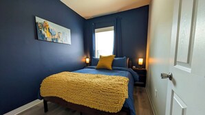 Un dormitorio con una cama, una mesita de noche, una lámpara y una ventana con cortinas.