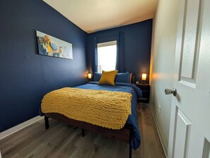 Een slaapkamer met een bed, nachtkastje, lamp en een raam met gordijnen.
