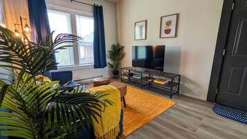 A living room with a sofa, a TV, a coffee table, and a large plant.