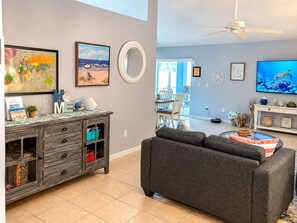 Ein Wohnzimmer mit einem grauen Sofa, einer Holzkabine mit Schubladen, einem Globus und einem Gemälde einer Strandlandschaft.