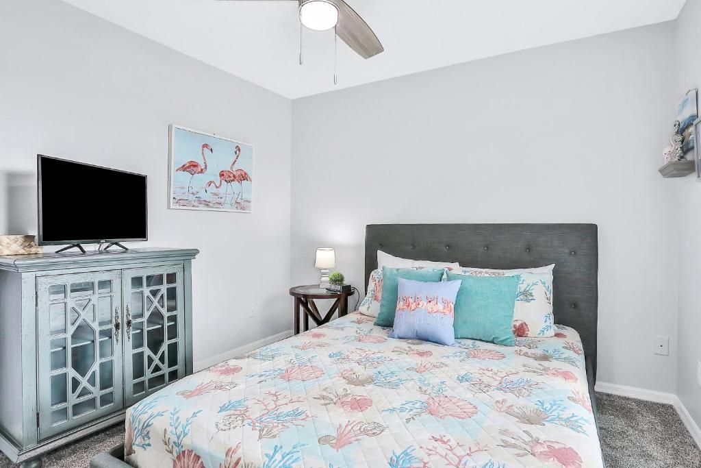 Um quarto com cama, televisão em um armário, ventilador de teto e uma parede com um quadro.