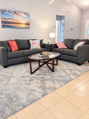 Ein Wohnzimmer mit einem grauen Ecksofa, einem Glastisch und einem gemusterten Teppich.