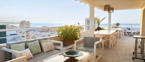 Une terrasse avec un espace salon, une table et une vue sur la mer.
