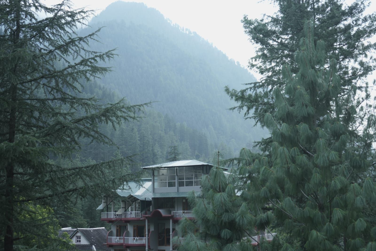 Ein zweistöckiges Gebäude mit Balkon, umgeben von dichtem Wald und einem Berg im Hintergrund.