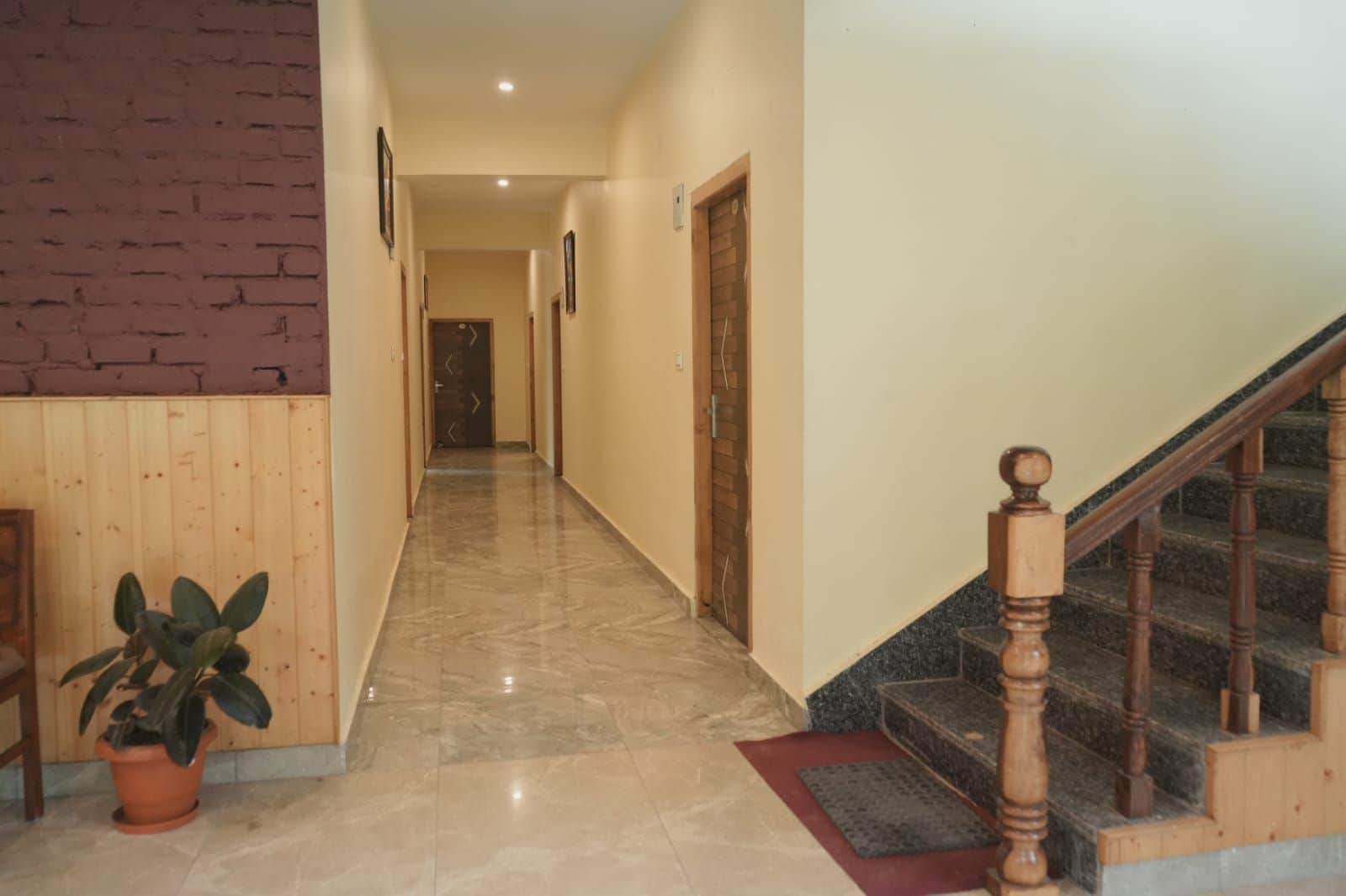 A hallway with a wooden staircase on the right, a potted plant on the left, and a door at the end.