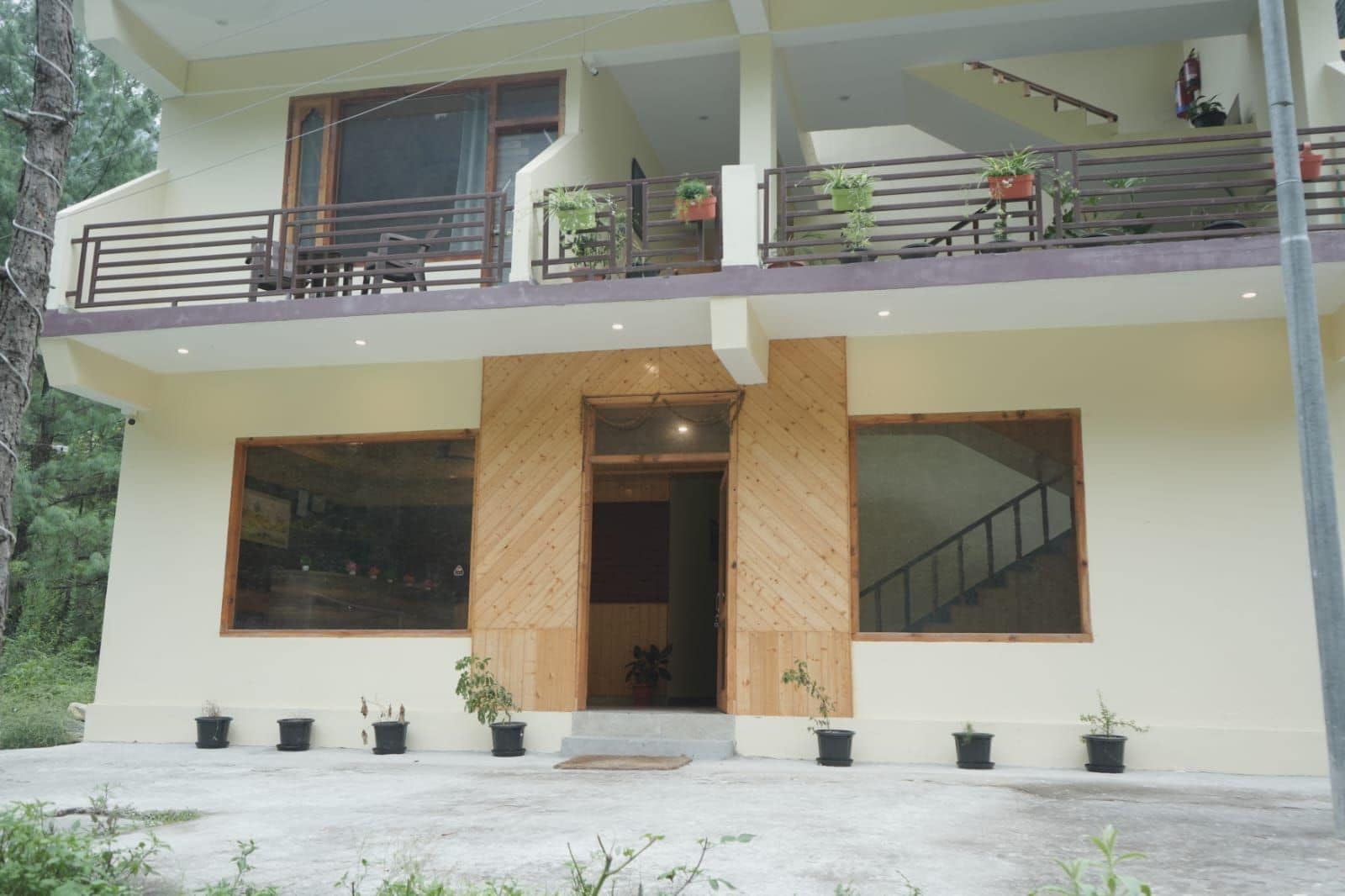 A two-story building with a balcony, large windows, and potted plants.