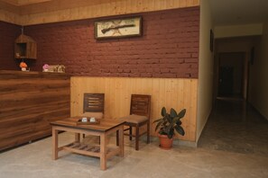 Un mostrador de recepción de madera con un banco y sillas, una planta en maceta y un reloj de pared.