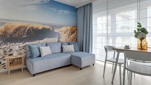 A modern living room with a sectional sofa, a dining table with chairs, and a large window. - Gdynia Comfort Apartment Żeromskiego 7 (Gdynia)