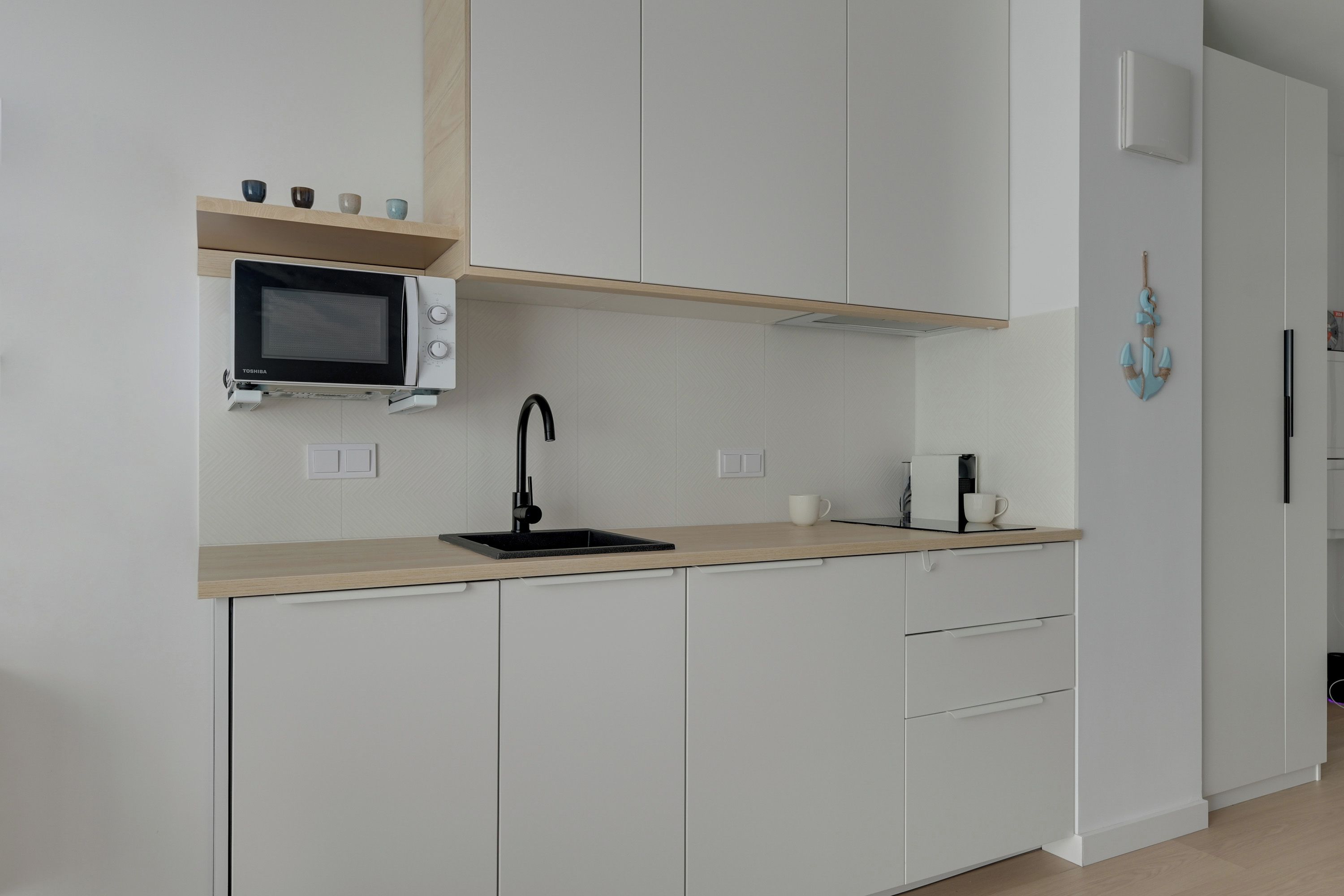 A modern kitchen with white cabinets, a black sink, a microwave, and a coffee machine.