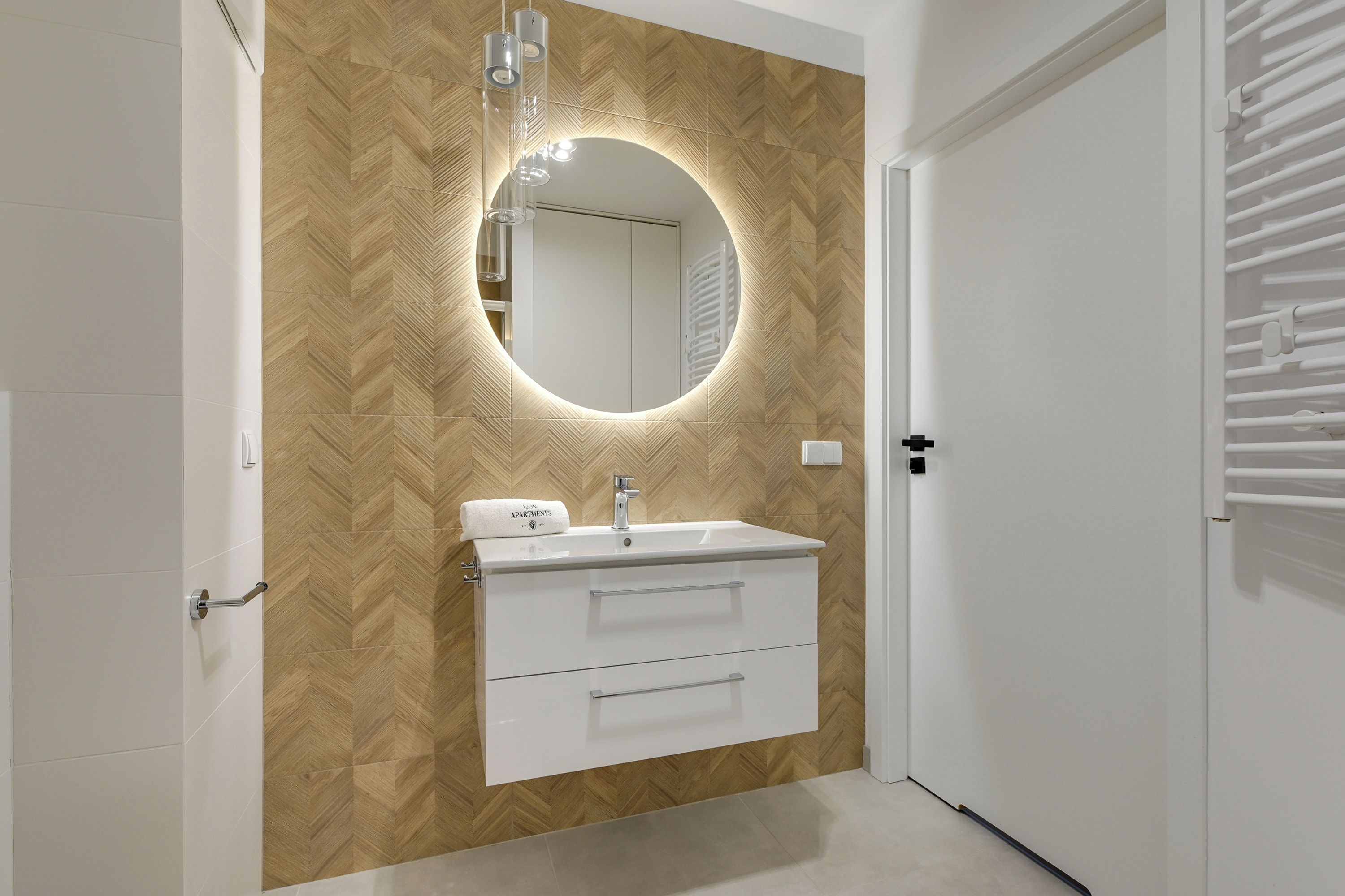 Een badkamer met een wand in herringbone-patroon, een wit wastafelmeubel met spiegel en een handdoek op het aanrecht.