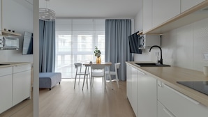 A modern kitchen with a dining area, white cabinetry, and a large window with curtains. - Gdynia Comfort Apartment Żeromskiego 7 (Gdynia)