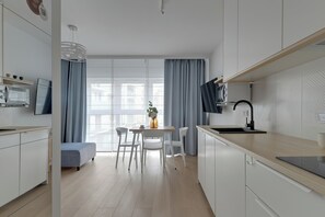 Cozinha moderna com área de refeições, armários brancos e uma grande janela com cortinas.