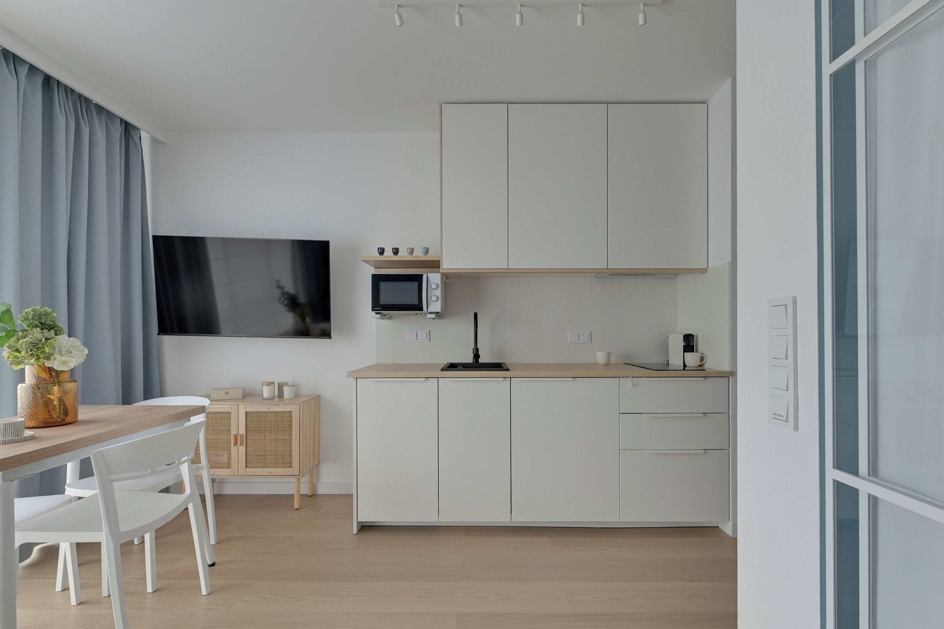 Una cocina moderna con armarios blancos, un microondas y un televisor de pantalla plana montado en la pared.