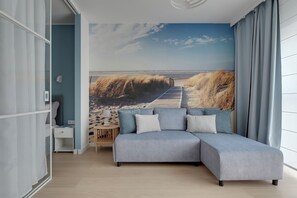 Ett modernt vardagsrum med en hörnsoffa, ett litet träbord och en väggmålning med strandtema.