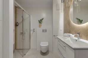 Casa de banho moderna com cabine de chuveiro em vidro, sanita branca e toucador com espelho.