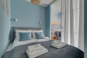 Quarto com cama, travesseiros, mesa de cabeceira e vista para o exterior.