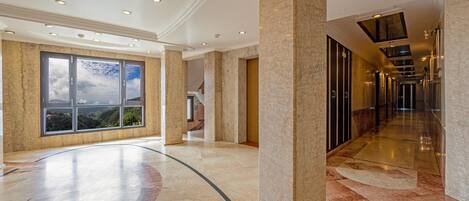 A spacious hotel lobby with a marble floor, large windows offering a view, and a long corridor leading to other areas.