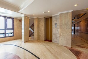 A spacious lobby with marble flooring, a staircase, and a digital elevator display.