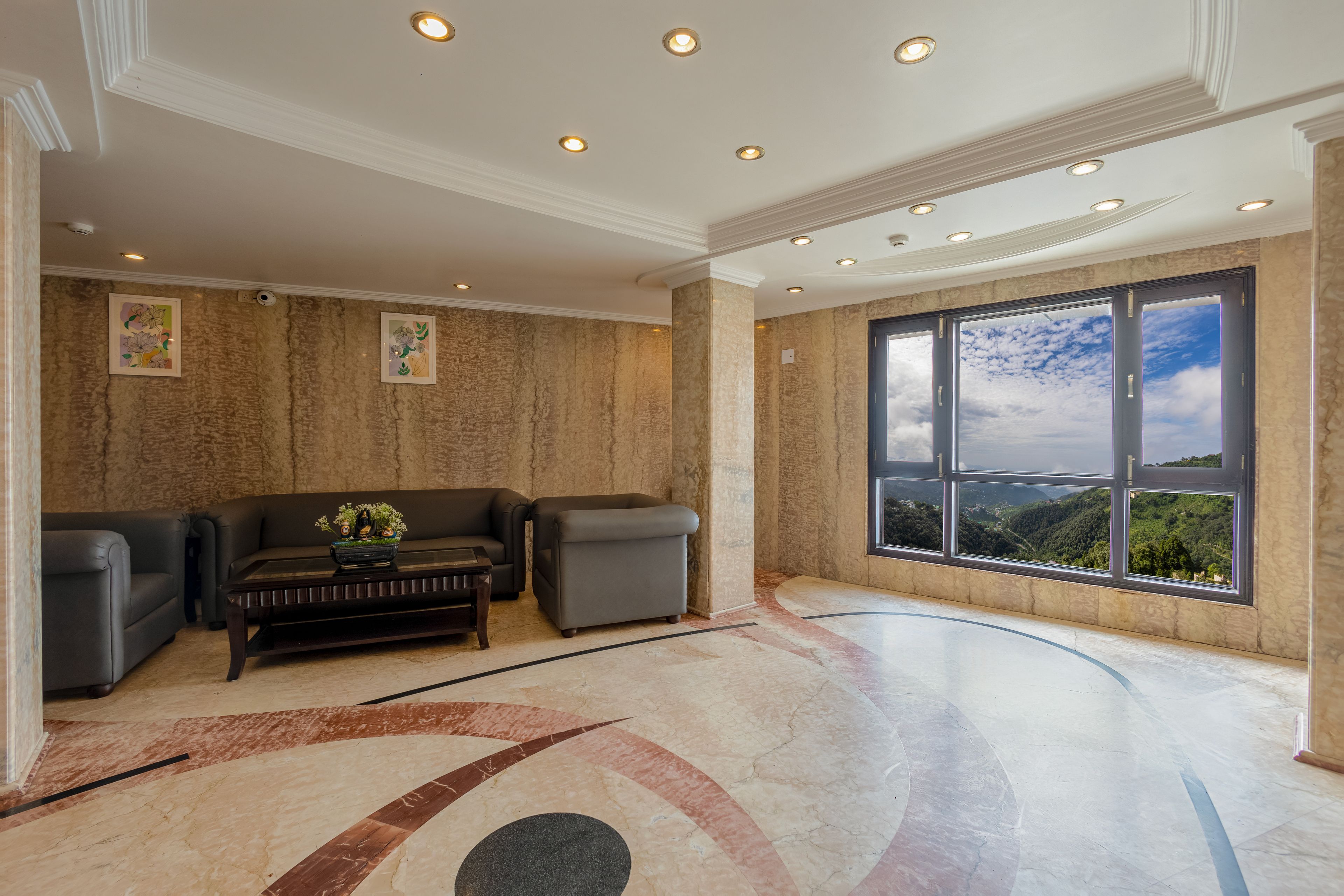 A spacious lobby with a marble floor, a sofa set, and a large window offering a view of a mountainous landscape.