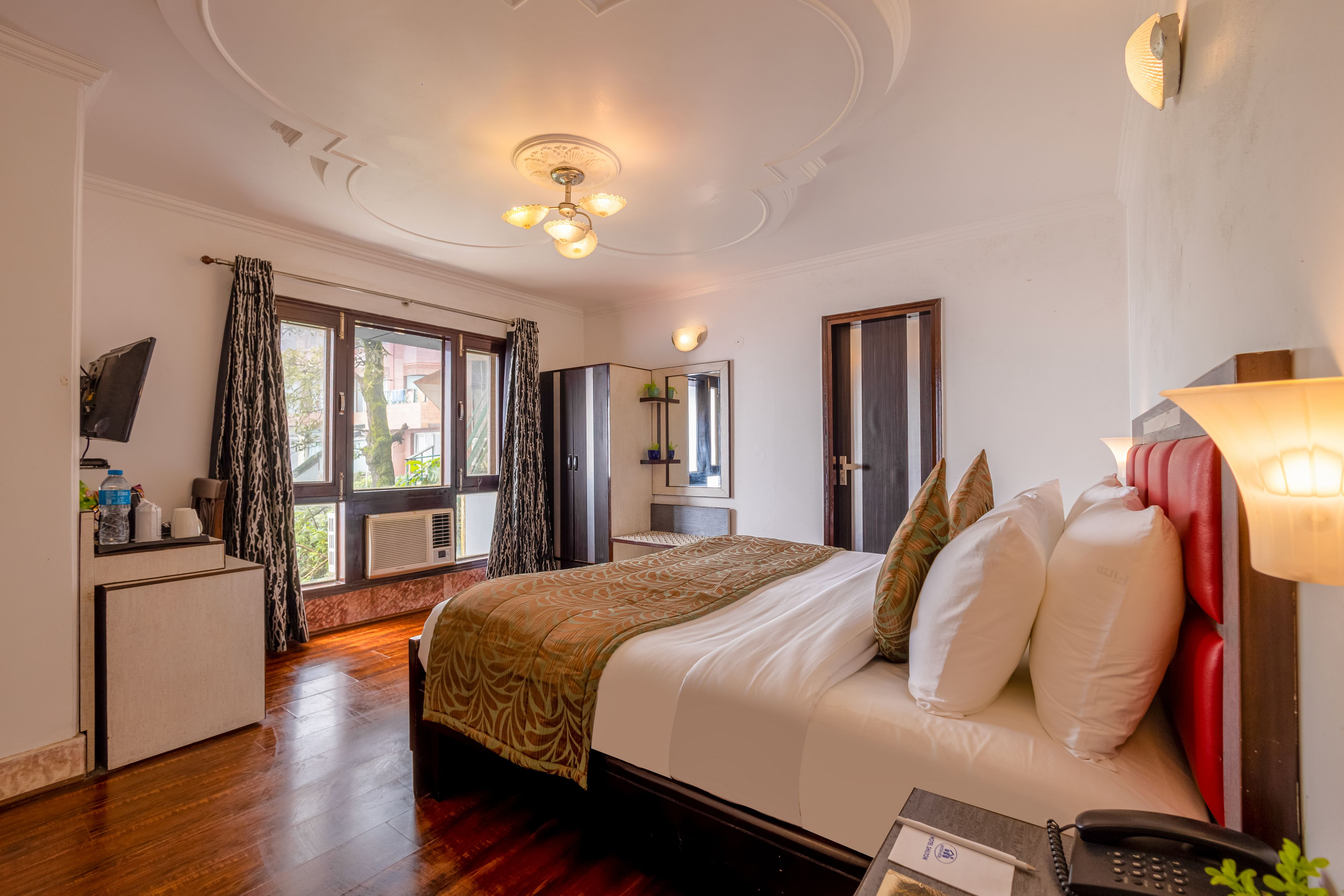 A hotel room with a bed, bedside table, lamp, and a view of the outdoors.