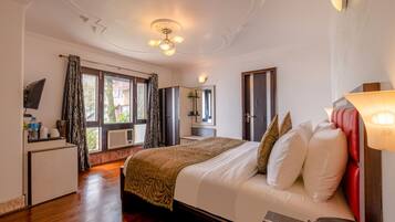 A hotel room with a bed, bedside table, lamp, and a view of the outdoors.