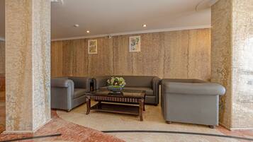 A modern lobby with a marble floor, a dark wooden coffee table, and two grey sofas.