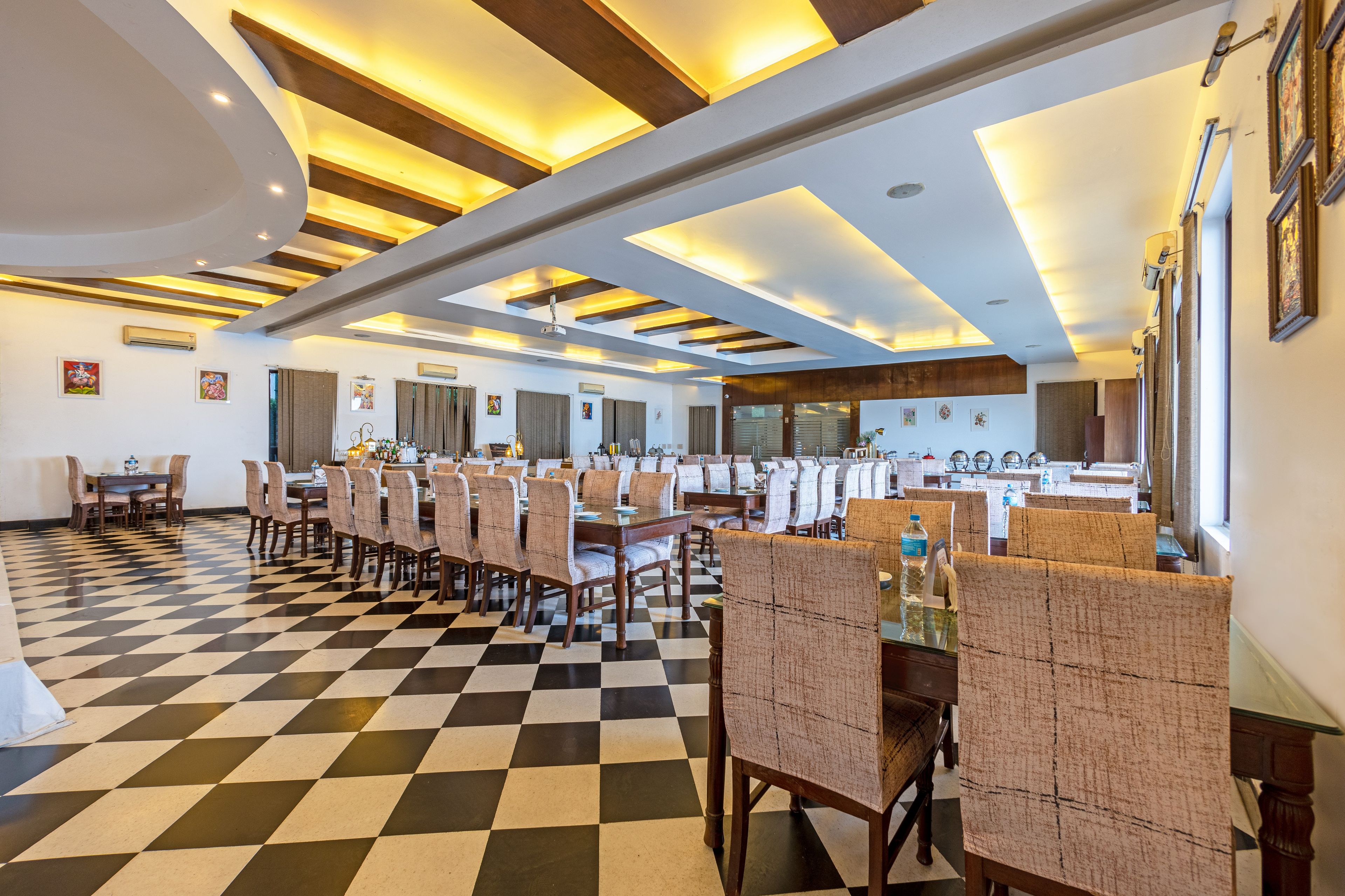 A hotel dining area with checkered flooring, multiple dining tables, and chairs.