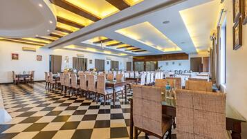 A hotel dining area with checkered flooring, multiple dining tables, and chairs.