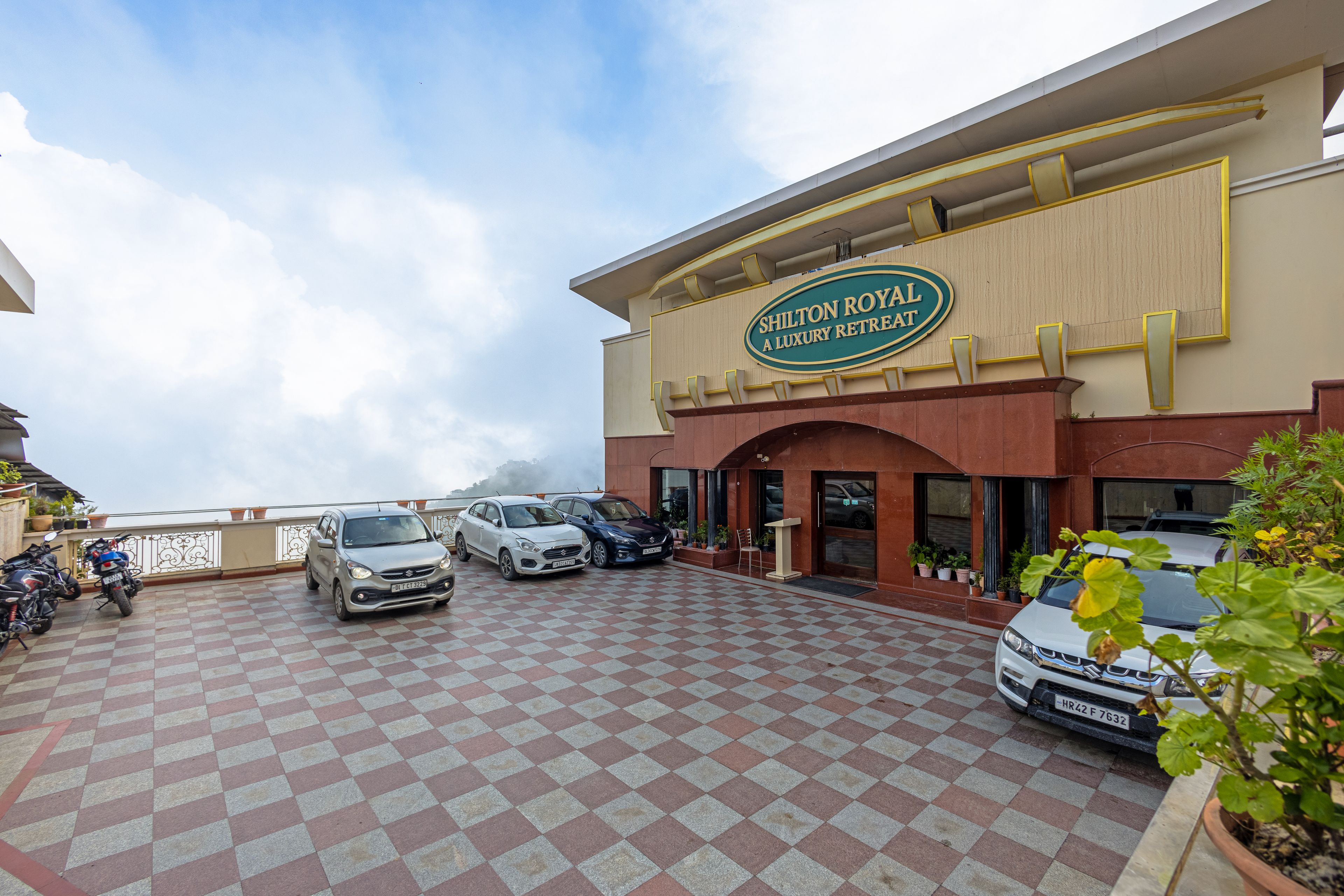 A hotel entrance with a checkered floor, parked cars, and a sign for 'Shilton Royal A Luxury Retreat'.