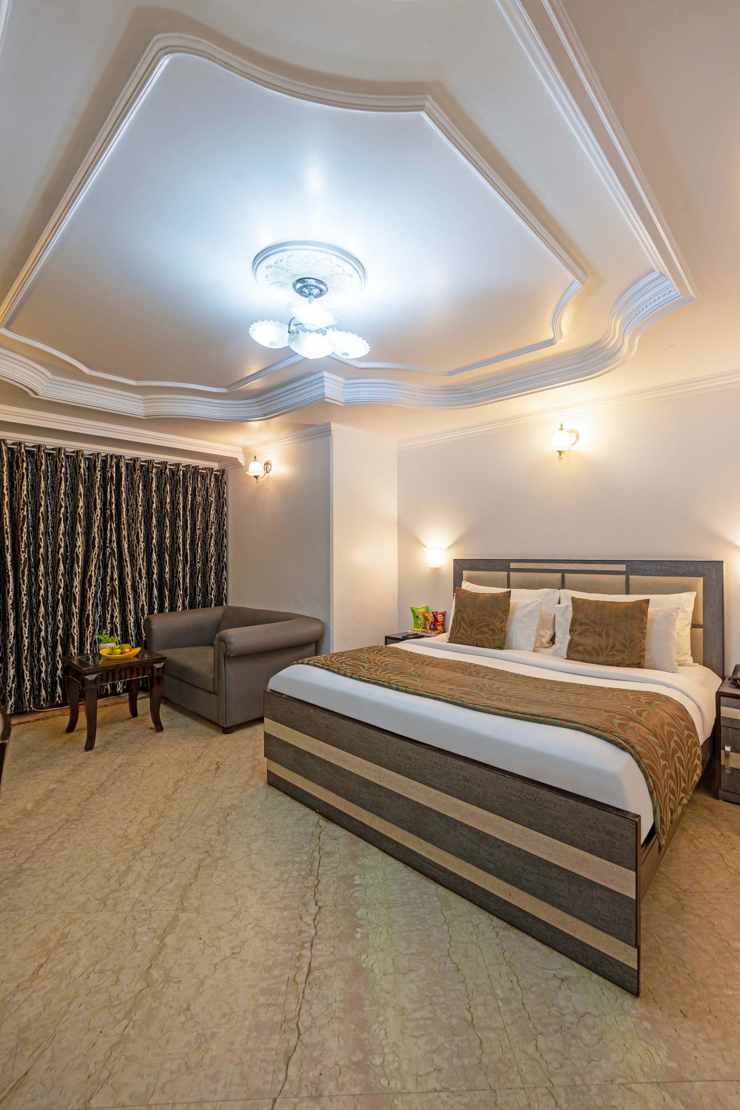 A hotel room with a large bed, a sofa, a small table with a bowl of fruit, and a patterned curtain.