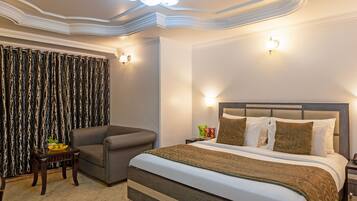 A hotel room with a large bed, a sofa, a small table with a bowl of fruit, and a patterned curtain.