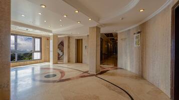 A spacious hallway with a marble floor, a large window offering a view of the outdoors, and a door with a number plaque.
