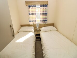 A twin room with two single beds, a bedside table with a lamp, and a window with striped curtains. - Beach Retreat (Southampton)