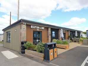 A reception and shop building with a wooden facade, a black door, and outdoor seating with umbrellas. - Beach Retreat (Southampton)