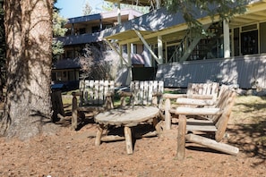 A wooden outdoor seating area with a table and chairs, surrounded by a wooden fence, with a building in the background. - Hi Country Haus Unit 1114 Downtown WP river view (Winter Park)