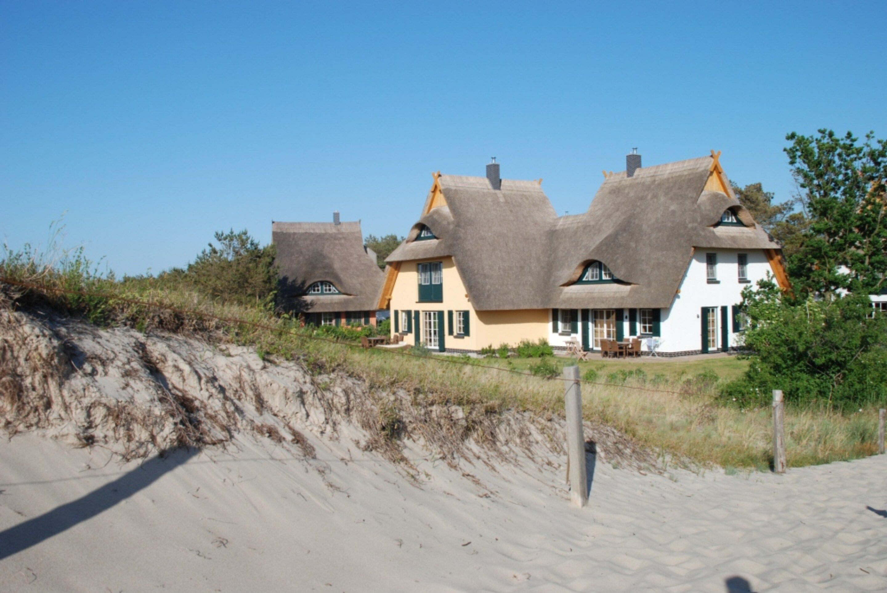 A row of traditional houses with thatched roofs, situated on a sandy beach with dunes in the foreground.