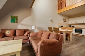 A cozy living area with a sofa, a small table, and a dining table with chairs. There is a kitchen with cabinets and a stove. - Maisonette Ferienwohnung, Dierhagen (Ostseebad Dierhagen)