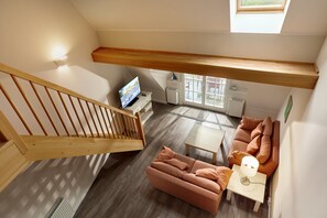 A loft-style living area with a wooden staircase, a sofa set, a television, and a small table. - Maisonette Ferienwohnung, Dierhagen (Ostseebad Dierhagen)