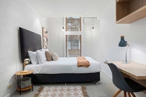 Een moderne slaapkamer met een bed, nachtkastje, lamp en een bureau met stoel.