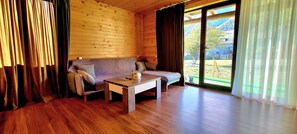 Une pièce de cabane en bois comprenant un canapé, une table basse et offrant une vue sur un paysage montagneux grâce à de grandes fenêtres.